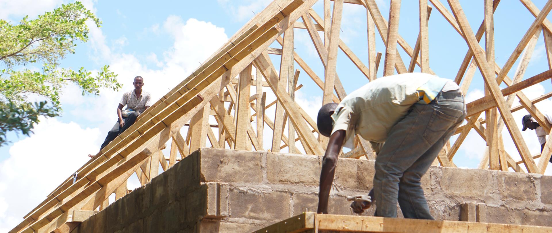 Dwaj mężczyźni zbijają gwoździami krokwie, tworząc zadaszenie budynku