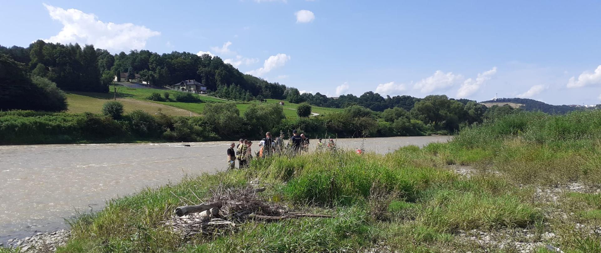 Grupa ratowników udziela pomocy osobie poszkodowanej na brzegu rzeki Dunajec