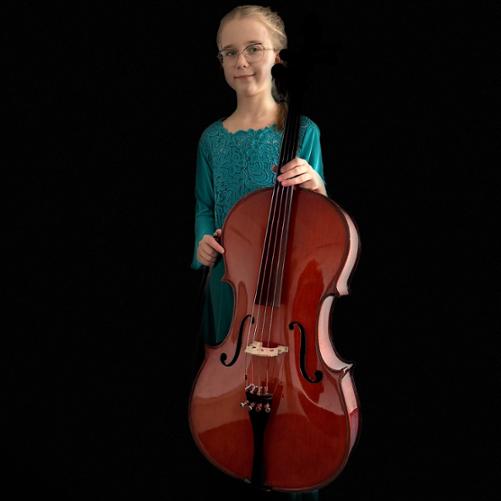 Uśmiechnięta dziewczynka w okularach na czarnym tle ubrana w turkusową sukienkę trzyma wiolonczelę. 