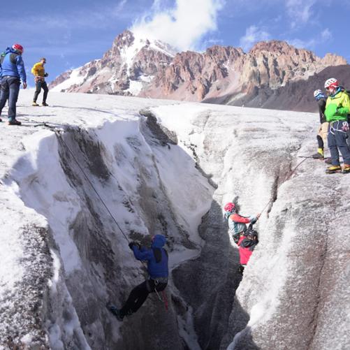Uczestnicy szkolenia przyglądają się trzem osobom schodzącym na linach do rozpadliny górskiej
