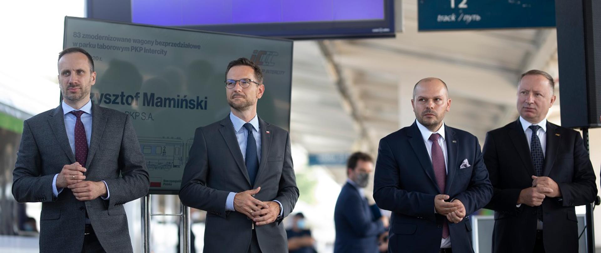 Na zdjęciu widać cztery osoby stojące na peronie kolejowym, wśród nich jest pan minister Waldemar Buda