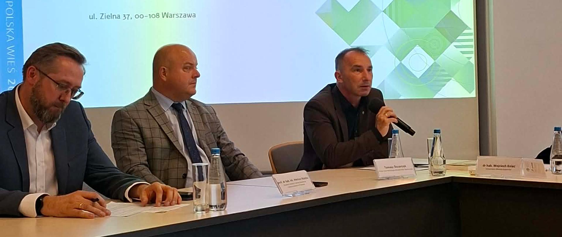 Trzej mężczyźni za stołem prezydialnym