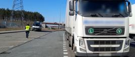 Na pierwszym planie przód ciężarówki zatrzymanej do kontroli drogowej przez ITD. W tle inspektor i radiowóz wielkopolskiej ITD.