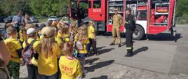 Dzieci na placu JRG w tle strażacy i samochód gaśniczy