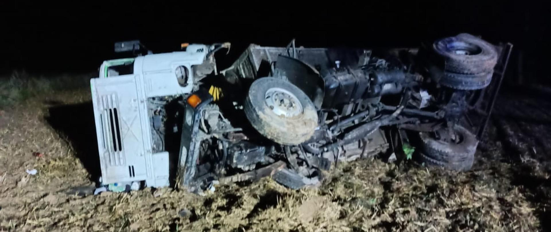 Na zdjęciu widoczny rozbity samochód ciężarowy, leżący na boku na polu ornym