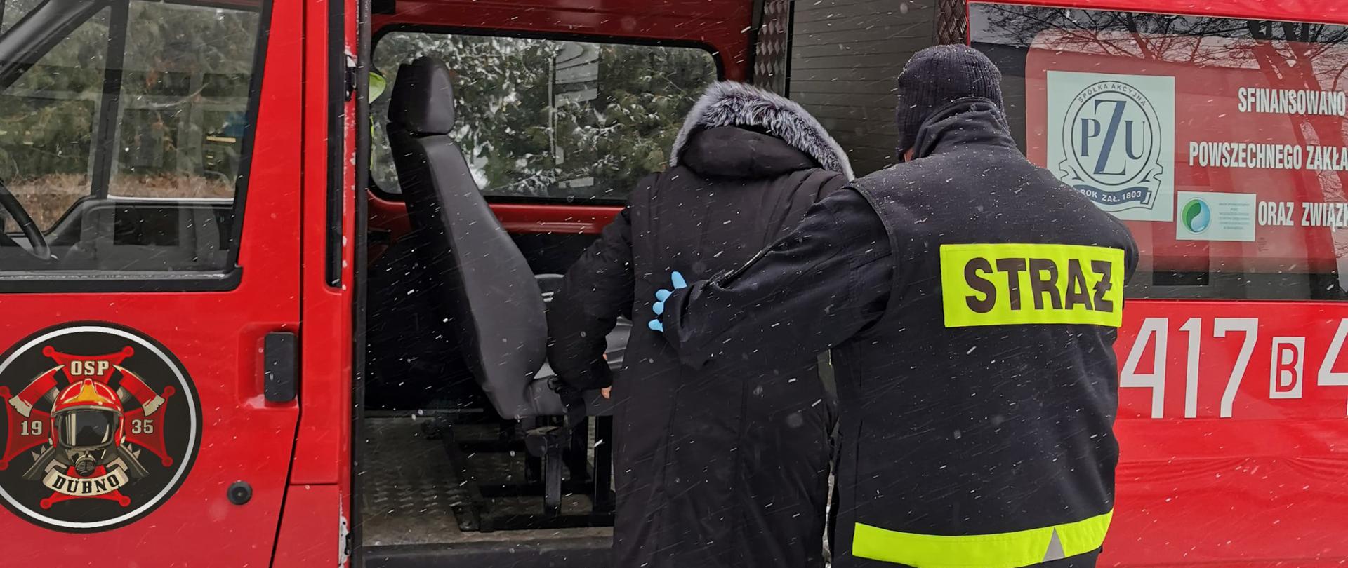 Strażak OSP Dubno pomagający wejść starszej osobie do samochodu pożarniczego w ramach pomocy w dotarciu do punktów szczepień osobom, które nie mogą tam dojechać we własnym zakresie. Działania prowadzone w ramach ogólnopolskiej akcji szczepień przeciw COVID-19