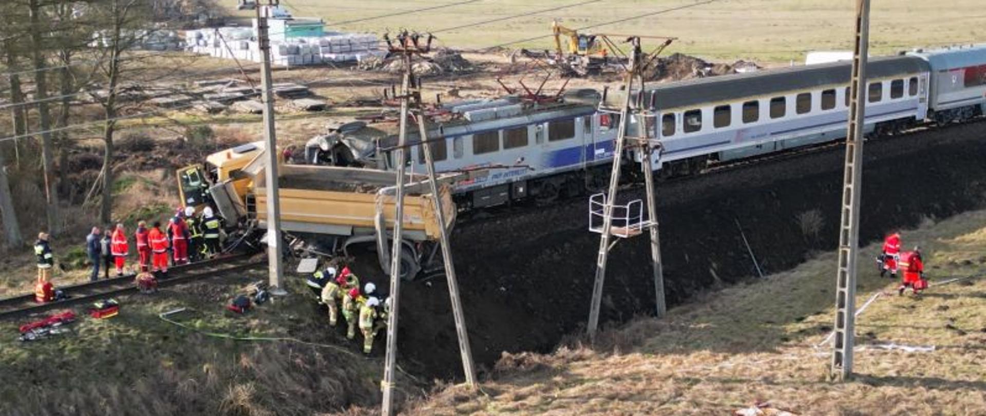 Zdjęcie wykonane z drona. Widać moment sprowadzania na noszach osoby poszkodowanej. Strażacy w kilka osób trzymają nosze i odprowadzają osobę do helikoptera.