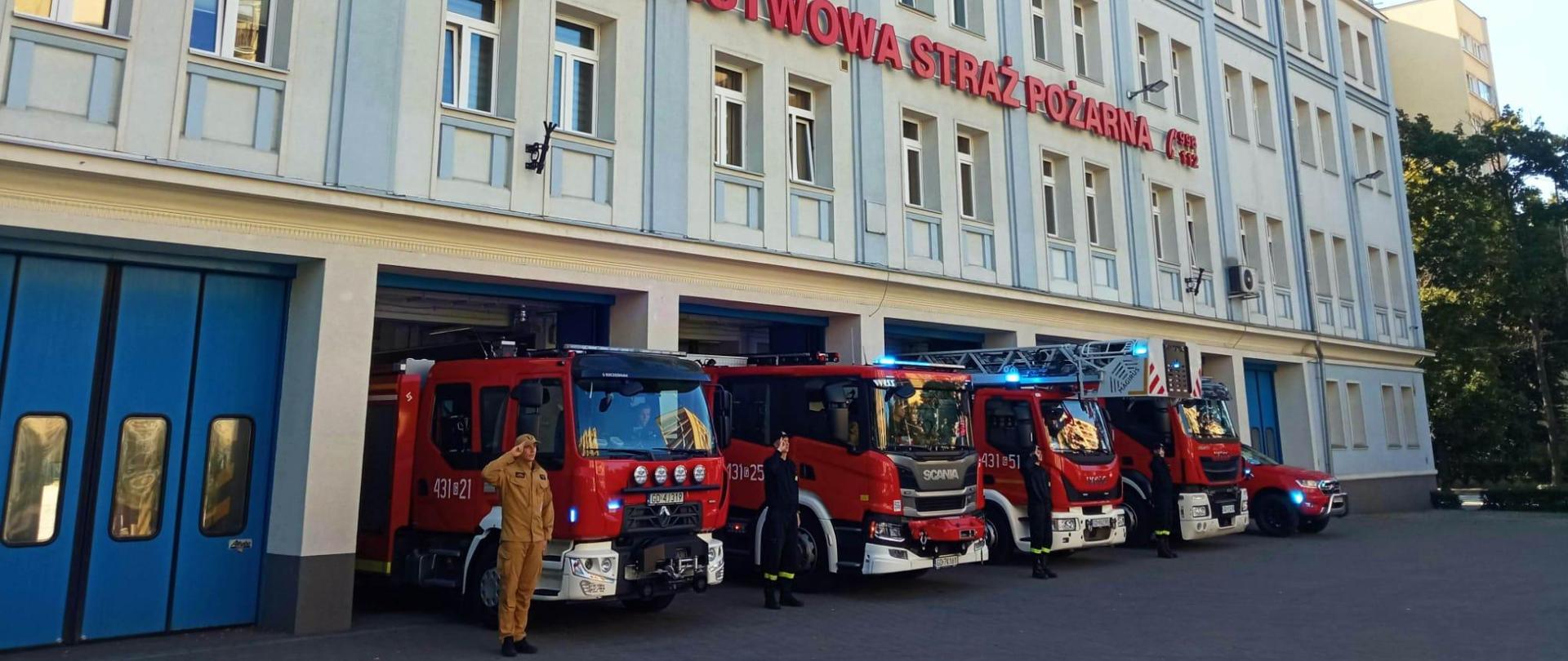Wozy strażackie w szyku, przed bramami jednostki Państwowej Straży Pożarnej