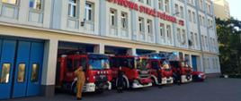 Wozy strażackie w szyku, przed bramami jednostki Państwowej Straży Pożarnej