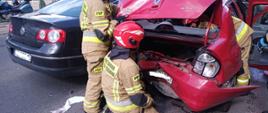 Na zdjęciu znajdują się rozbite auta oraz strażacy którzy wykonują dostęp do pojazdu. 