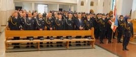 Na zdjęciu widzimy strażaków podczas mszy św. Z okazji dnia strażaka. Widzimy poczty sztandarowe i kompanie honorowa KM PSP w Tarnowie. Wszyscy umundurowani w mundury galowe przed nimi na ławce położone są czapki rogatywki.