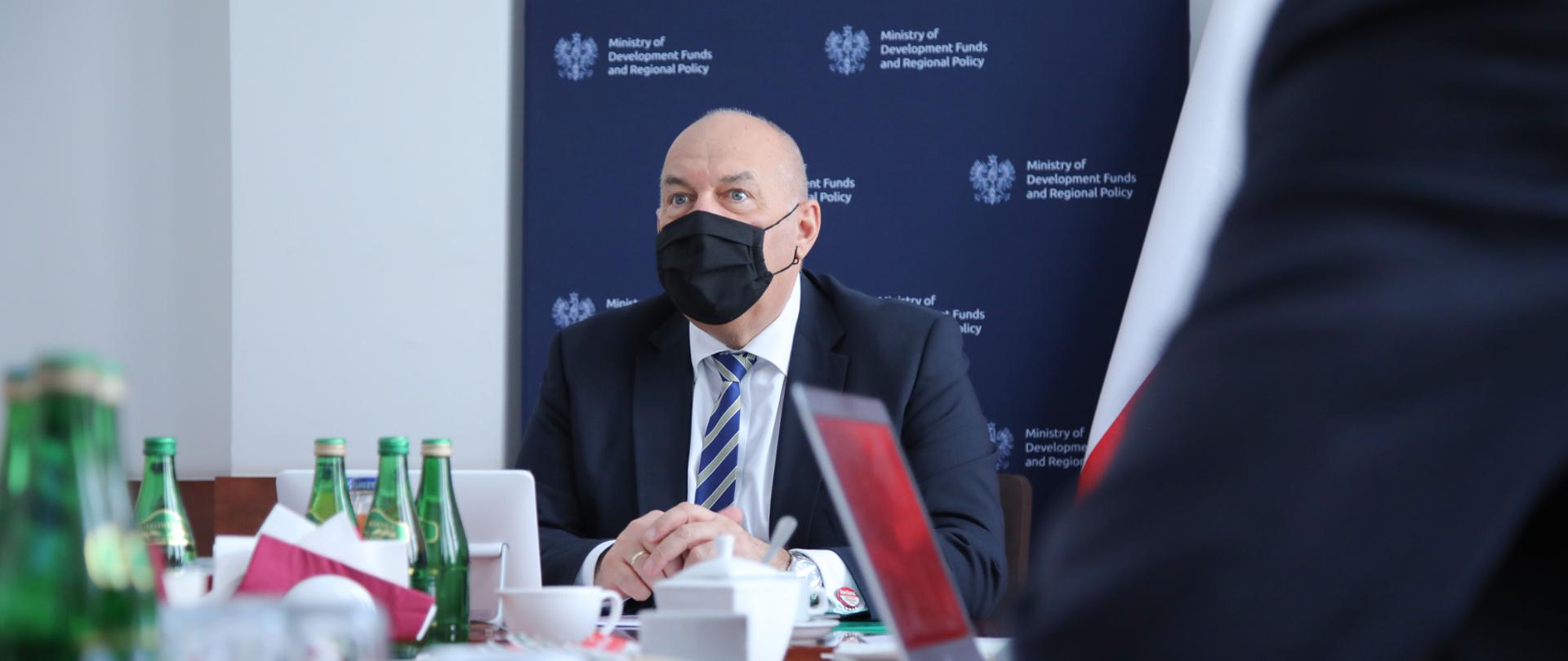 Minister Kościński siedzi przy stole podczas wideokonferencji