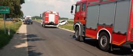Zdjęcie przedstawia dwa wozy ratowniczo-gaśnicze straży pożarnej oraz dwa rozbite samochody osobowe, jeden w przydrożnym rowie drugi na jezdni 
