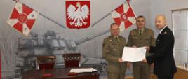 Komendant Powiatowy wraz z Dowódcą 11MPA i Szefem Delegatury na sali tradycji w JW trzymają podpisane porozumienie. 