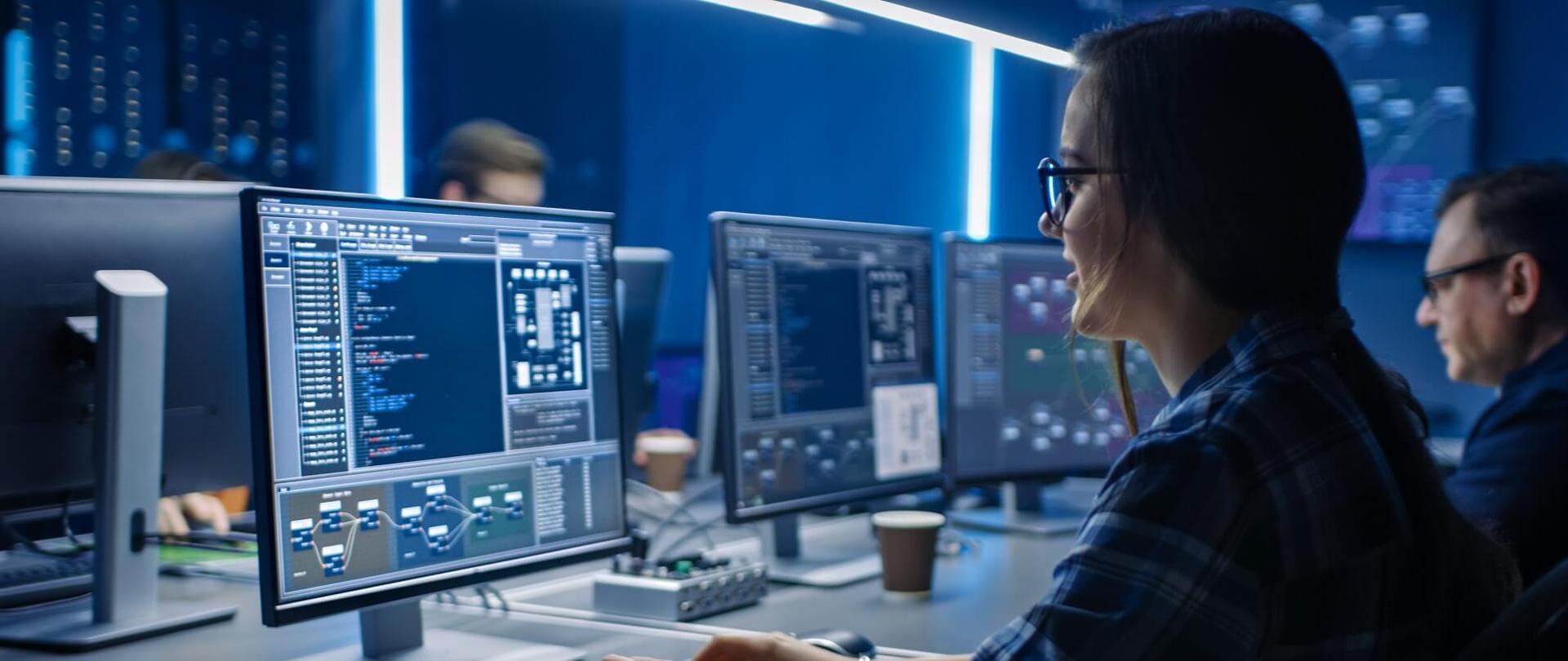 Na pierwszym planie kobieta pracująca przy komputerze
