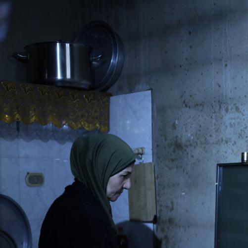 Kobieta w hidżabie stoi obok kuchenki gazowej, na palniku której stoi duże naczynie