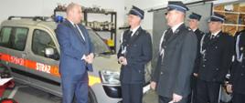 Przekazanie samochodu w OSP Jutrosin. Garaż w remizie OSP Jutrosin. Minister Dziedziczak na tle przekazywanego samochodu w towarzystwie naczelnika OSP i kierowcy, którym przed chwilą wręczył kluczyki i dowód rejestracyjny. W tle regał ze sprzętem, z prawej strony trzech druhów OSP.