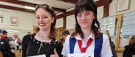 Na zdjęciu widzimy dwie uczennice: Maja Sochacka z kl. 4A i Patrycja Grad z kl. 4B - Laureatki VIII. Powiatowego Konkursu Języka Angielskiego:. Fot.: Monika Cholewa. Maja ubrana jest w czarną bluzkę, ma ciemne rozpuszczone włosy do ramion. Ciemne słoneczne okulary pełnią funkcję opaski na włosy. Maja w prawej ręce trzyma dyplom świadczący o zdobyciu pierwszego miejsca w konkursie. Lewą rękę z kciukiem podnosi do góry Uczennica ma założone długie spodnie w kratkę czarno-białą i sportowe adidasy. Po prawej stronie widzimy drugą uczennicę - Patrycję Grad. Patrycja również w rękach trzyma dyplom konkursowy. Uczennica ubrana jest kolorowo w barwach flagi angielskiej. Dominują kolory niebieski, biały i czerwony. Patrycja ma założoną białą koszulę z krótkim rękawem, niebieską kamizelkę i czerwony krawat. Dodatkowo spodnie uszyte są z elementów flagi Wielkiej Brytanii. (popularnie zwana Union Jack) jest połączeniem flagi niebieskiej z czerwonym Krzyżem św. Jerzego (patrona Anglii) w białym obramowaniu, oraz nakładających się nakładające się na siebie krzyży: czerwony św. Patryka (patrona Irlandii) i biały św. Andrzeja (patrona Szkocji).