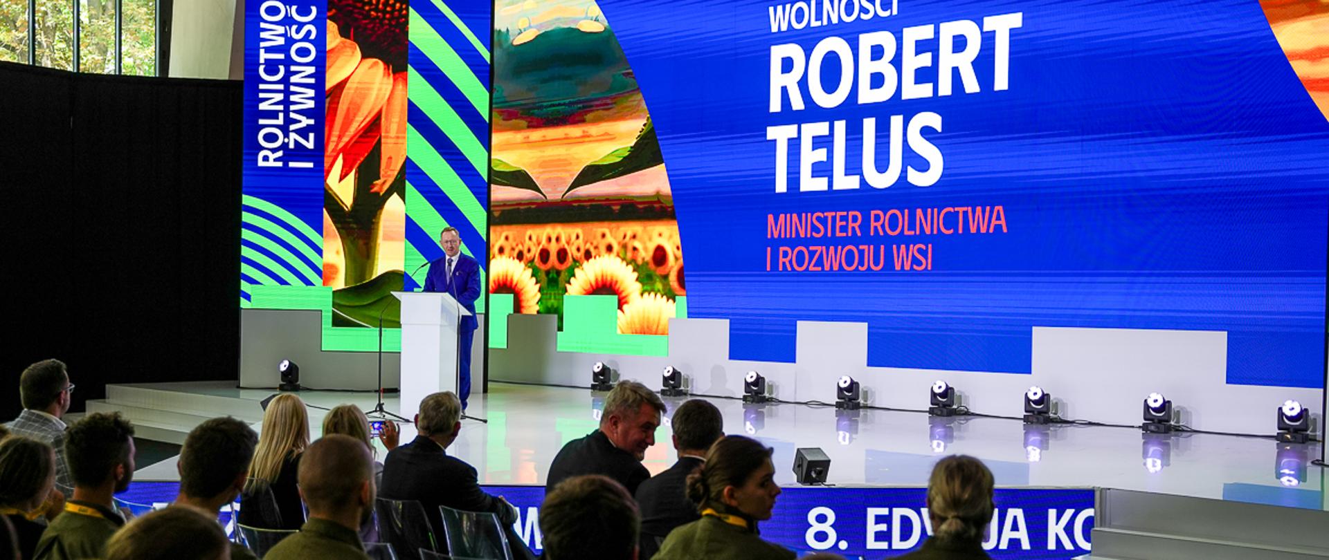 Minister Robert Telus stojący na scenie przy mównicy
