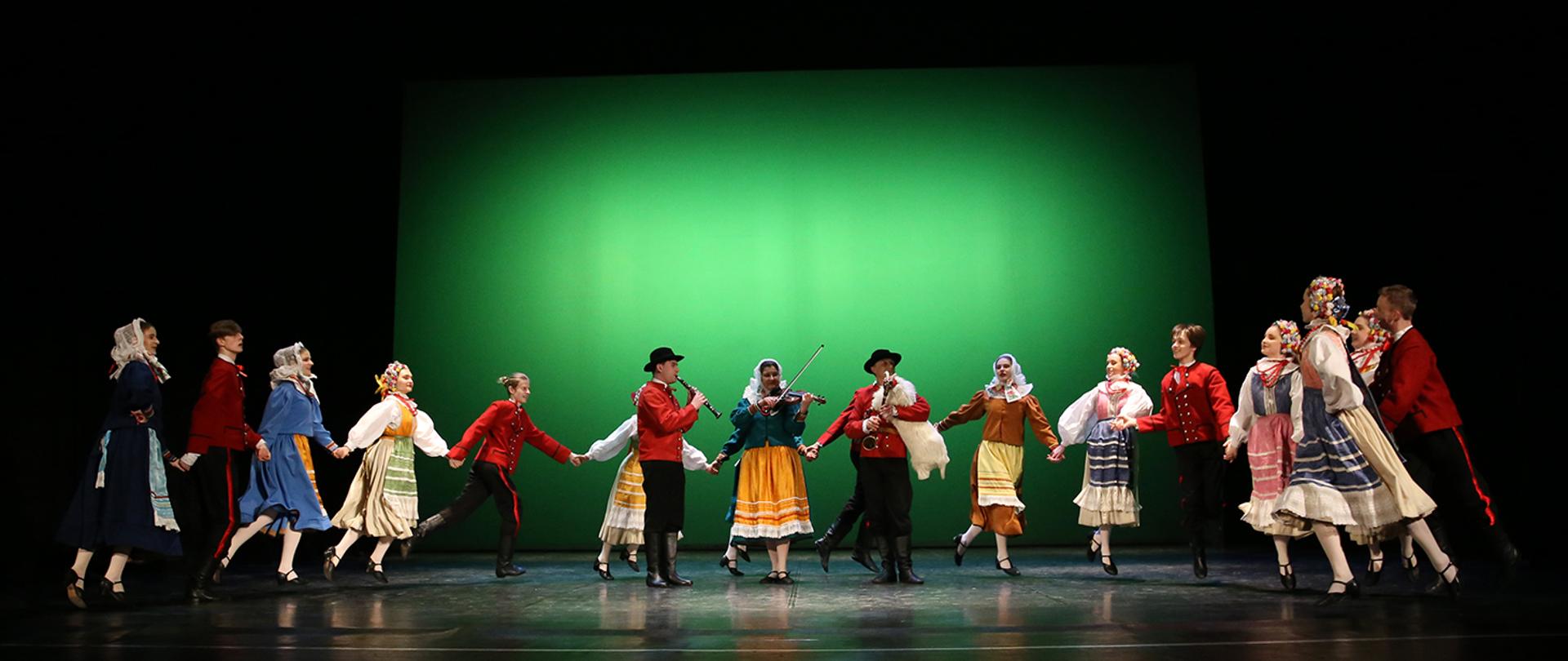Scena, zielone tło, tancerze w strojach ludowych