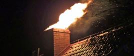 Na zdjęciu przedstawiony jest dach budynku wraz z kominem, z którego wydobywa się ogień oraz iskry. Zdjęcie zrobione w nocy, dookoła panuje mrok.
