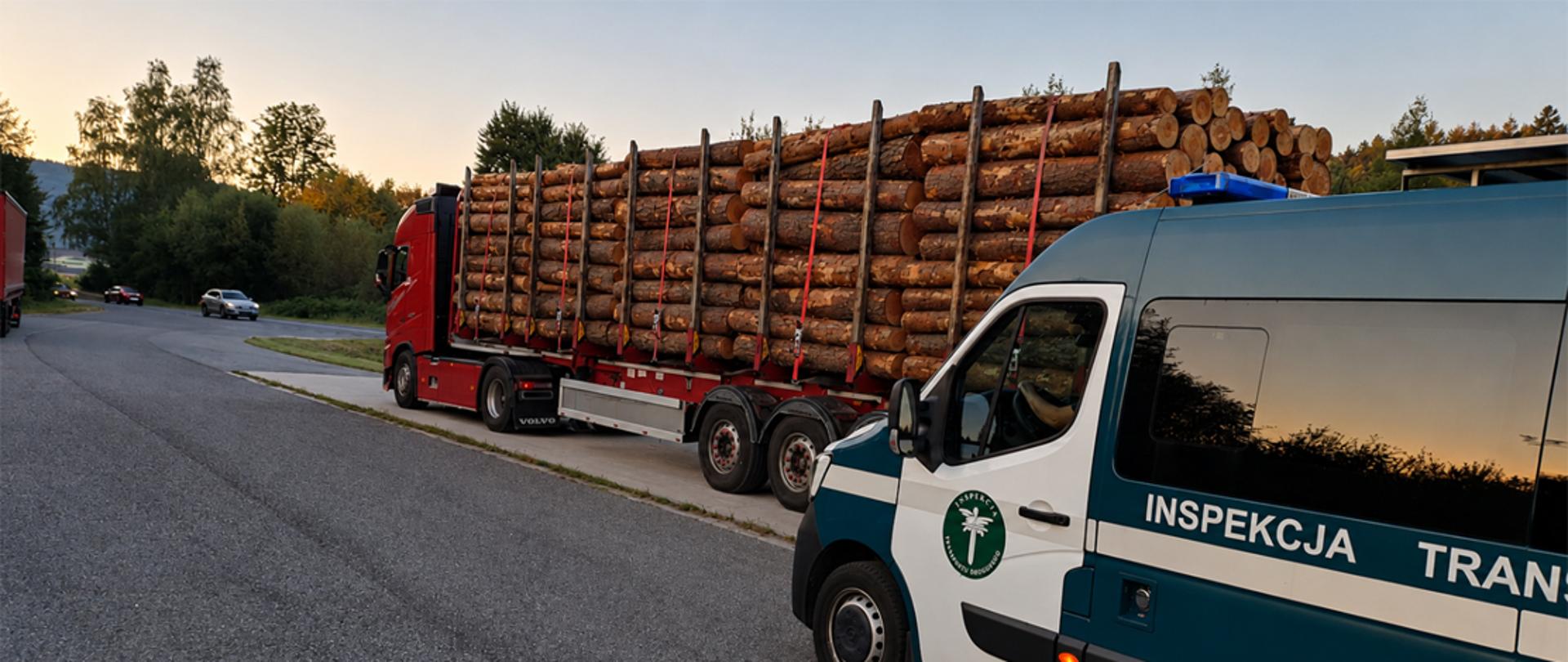 Pojazd Inspekcji Transportu Drogowego podczas kontroli ciężarówki przewożącej drewno przy drodze o zmierzchu