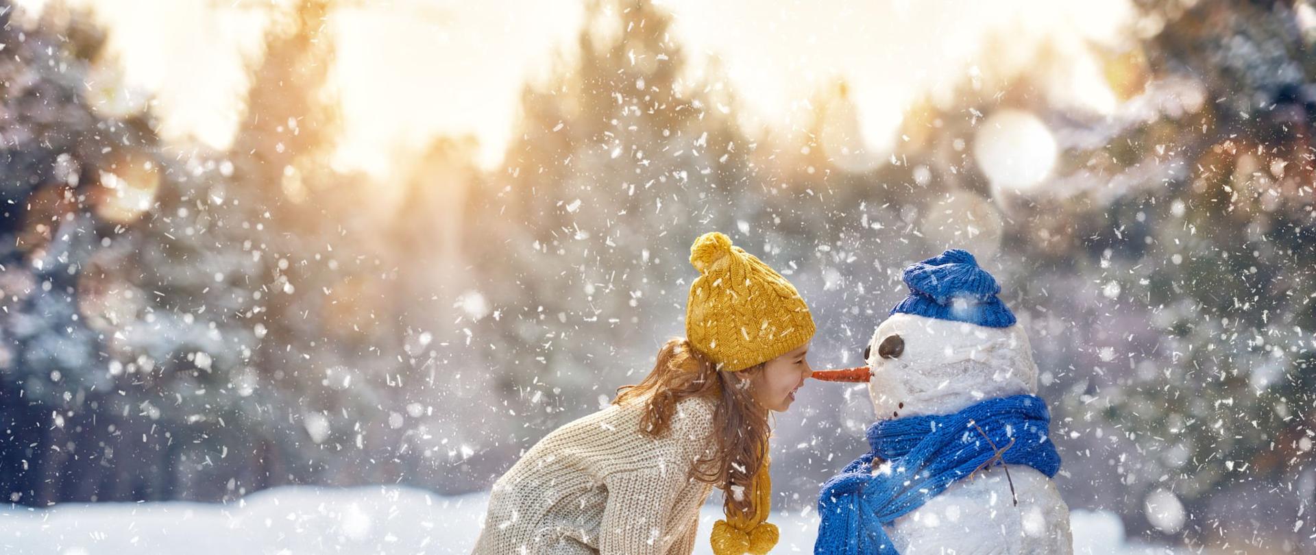 happy child girl plaing with a snowman on a snowy winter walk
