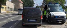 Zatrzymany do kontroli stanu trzeźwości kierowca busa i stojący obok oznakowany radiowóz ITD typu furgon.