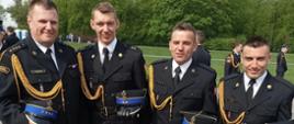 Na zdjęciu widać czterech strażaków w umundurowaniu galowym. Strażacy znajdują się na placu podczas obchodów dnia strażaka w Warszawie. 