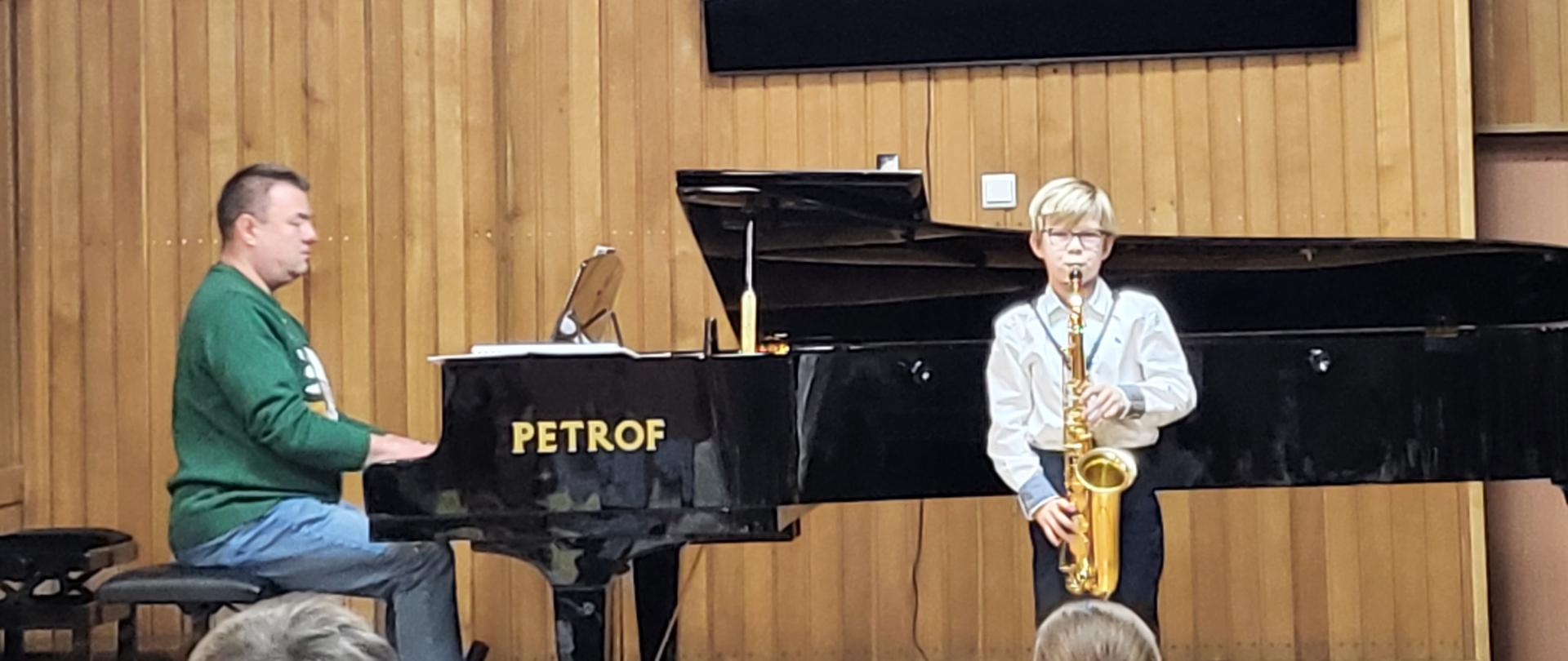 grafika przedstawia nauczyciela oraz ucznia klasy pierwszej grającego na instrumencie dętym