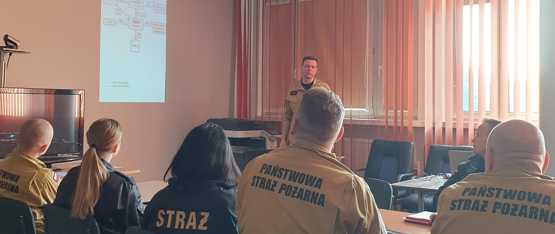 Zdjęcie w pomieszczeniu. Widać funkcjonariuszy. Światło naturalne. Na podłodze dywan.