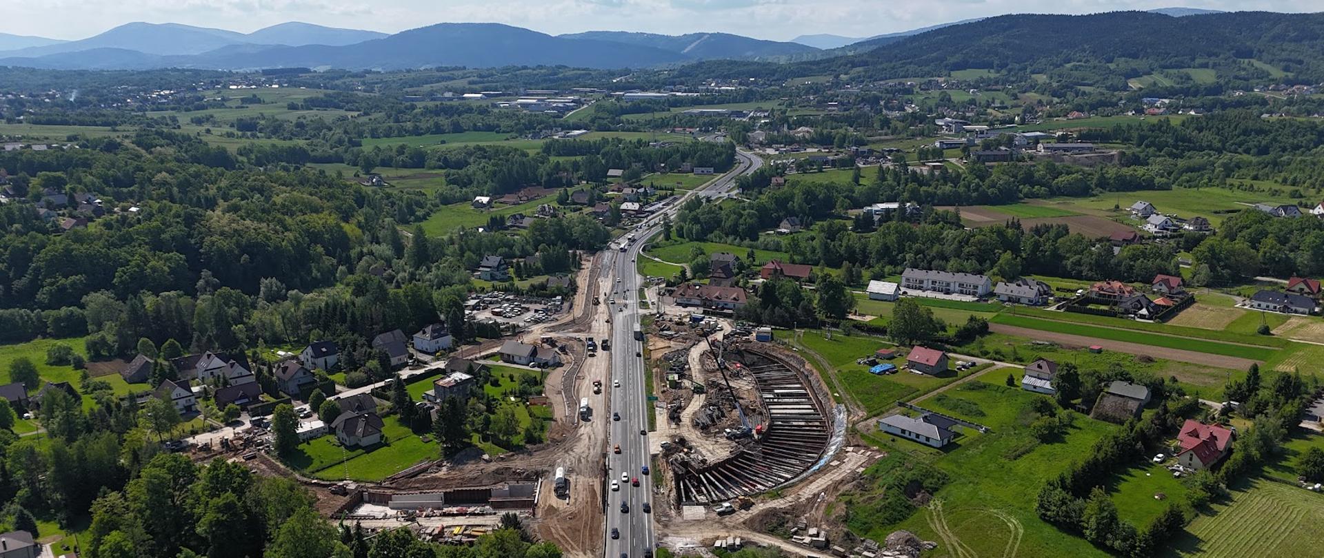 Zakopianka w Krzyszkowicach, widoczna budowa węzła i przejazdu pod DK7, wokół trasy zabudowania i zadrzewienia, w oddali Beskidy