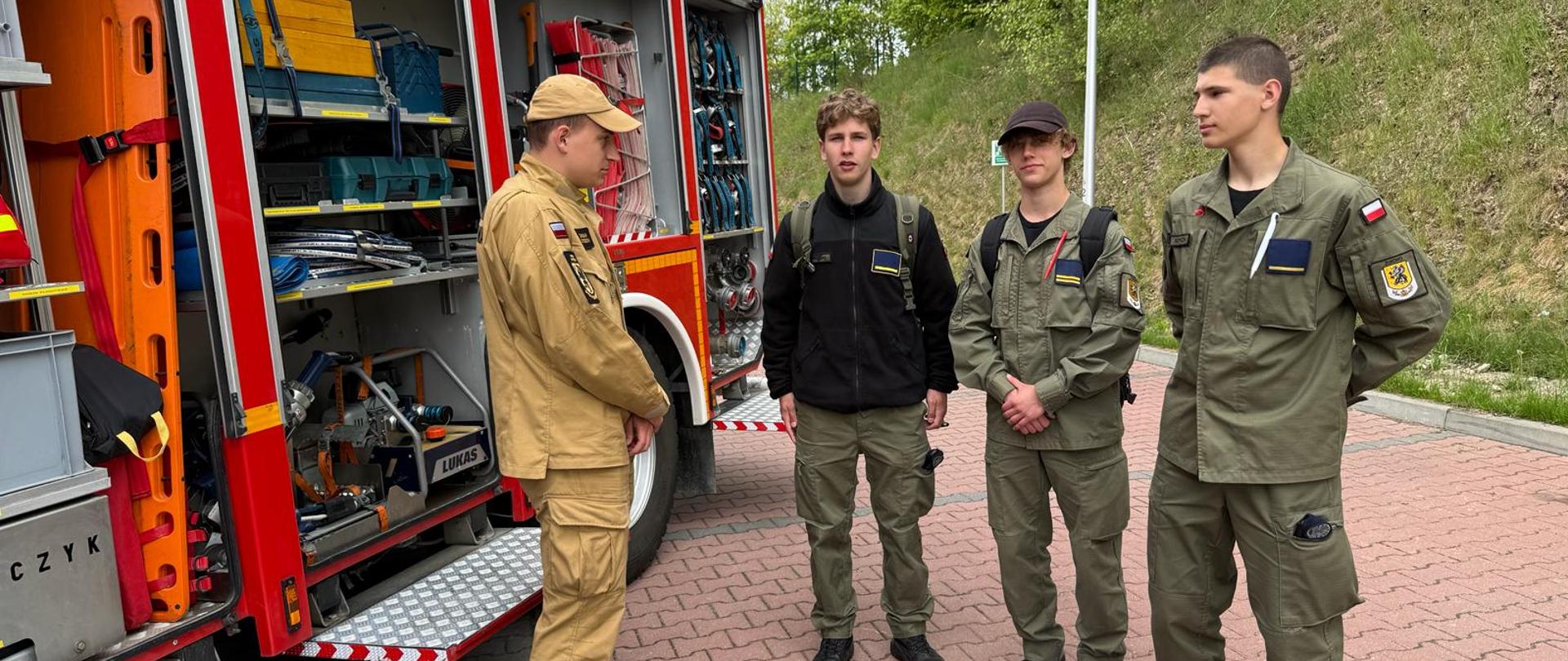 Zdjęcie przedstawia strażaka prezentującego zainteresowanym samochód ratowniczo-gaśniczy.