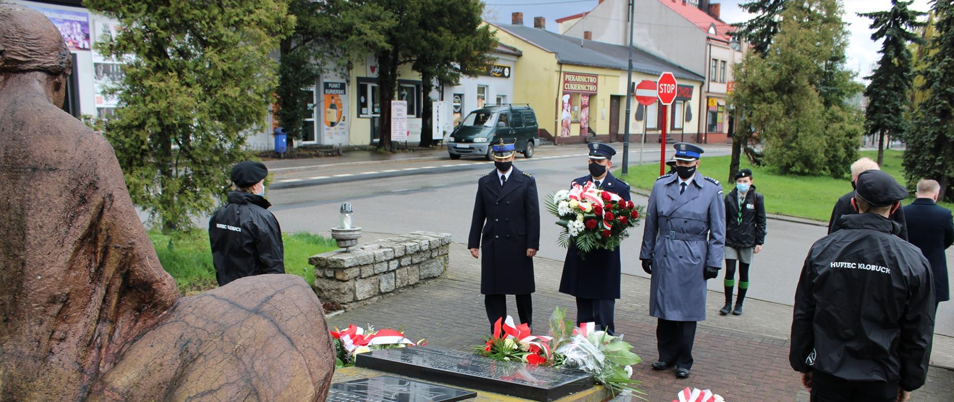 Zdjęcie przedstawia uroczyste złożenie kwiatów pod pomnikiem Matki Polki w Kłobucku przez przedstawicieli służb mundurowych powiatu kłobuckiego.
