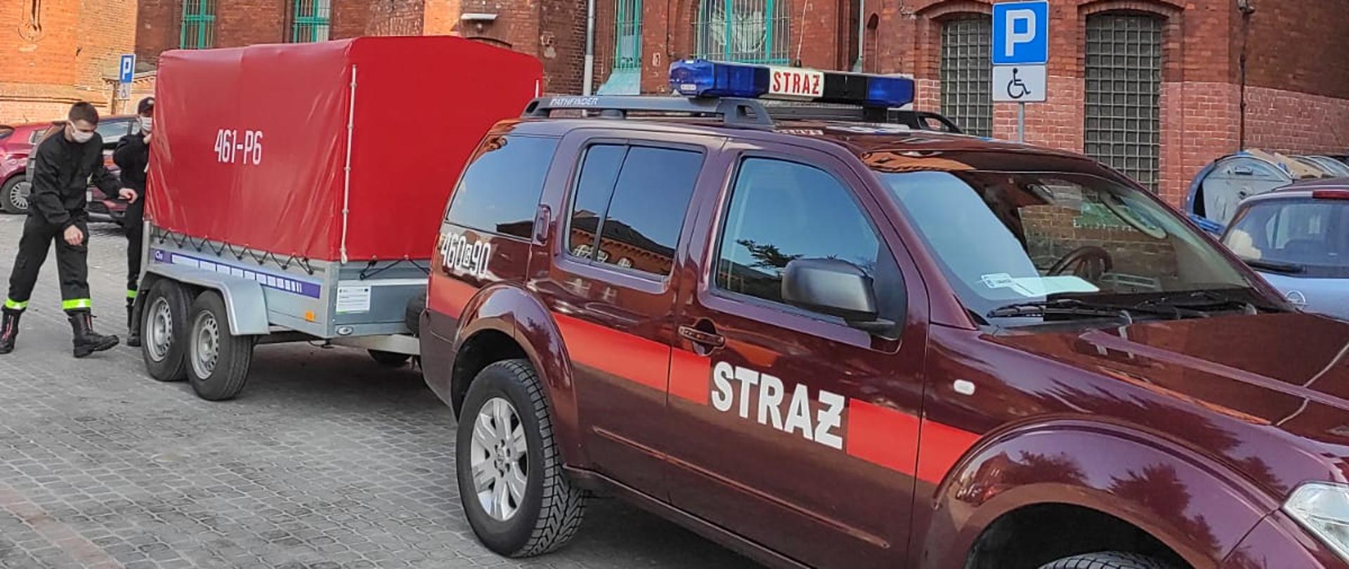 Na zdjęciu samochód terenowy z przyczepką podczas wyładunku maseczek.