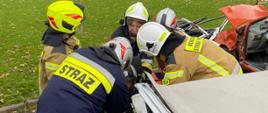 strażacy podczas próby ewakuacji osoby poszkodowanej z samochodu osobowego
