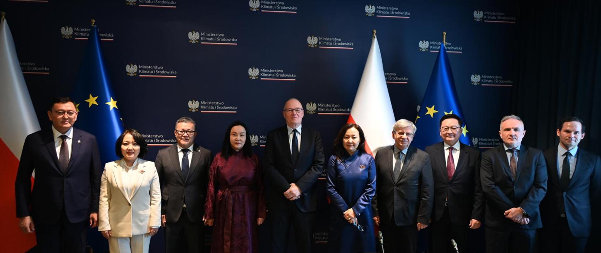 Deputy Minister Krzysztof Galos, Chief Geologist of Poland, during a meeting with a delegation of the Mongolian-Polish Parliamentary Group of the State Great Khural of Mongolia, led by its chairman, Jargalsaikhan Zoljargal, and the Mongolian Ambassador to Poland, Oyundari Navaan-Yunden. The photo shows ten people standing in front of a backdrop displaying the logos of the Ministry of Climate and Environment, all looking at the camera. On the right and left sides of the image, there are the flags of Poland and the European Union.