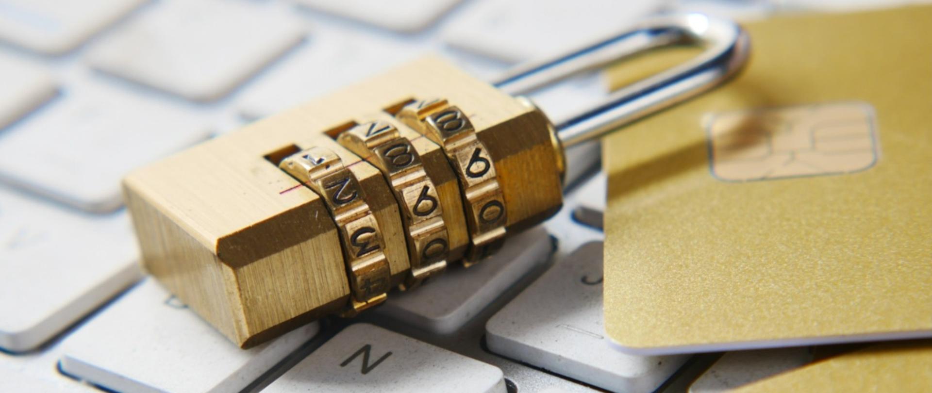 Klawiatura komputera. Leżą na niej zamknięta kłódka i karta bankomatowa.