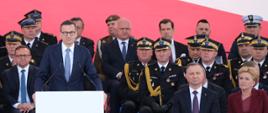 Widok z góry na strażaków stojących na placu oraz na trybunę z gośćmi, przemawia do mikrofonu premier RP