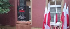 Na tle ściany budynku znajduje się pomnik - bryła w kolorze czarnym. Na jej szczycie umieszczone jest godło RP, a w centralnej części napis: Pamięci działaczy NSZZ Solidarność represjonowanych w czasie stanu wojennego 1982-1983 w Wojskowym Obozie Internowania w Rawiczu. Instytut Pamięci Narodowej. Z prawej strony stoi stojak z flagami biało-czerwonymi.