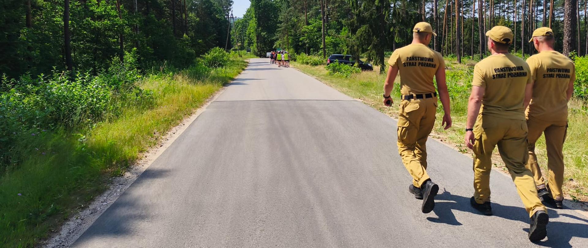 Fotografia przedstawia funkcjonariuszy idących drogą leśną a przed nimi idą uczestnicy obozu sprawdzając drogę ewakuacyjną do miejsca schronienia w przypadku niebezpiecznych zjawisk pogodowych.