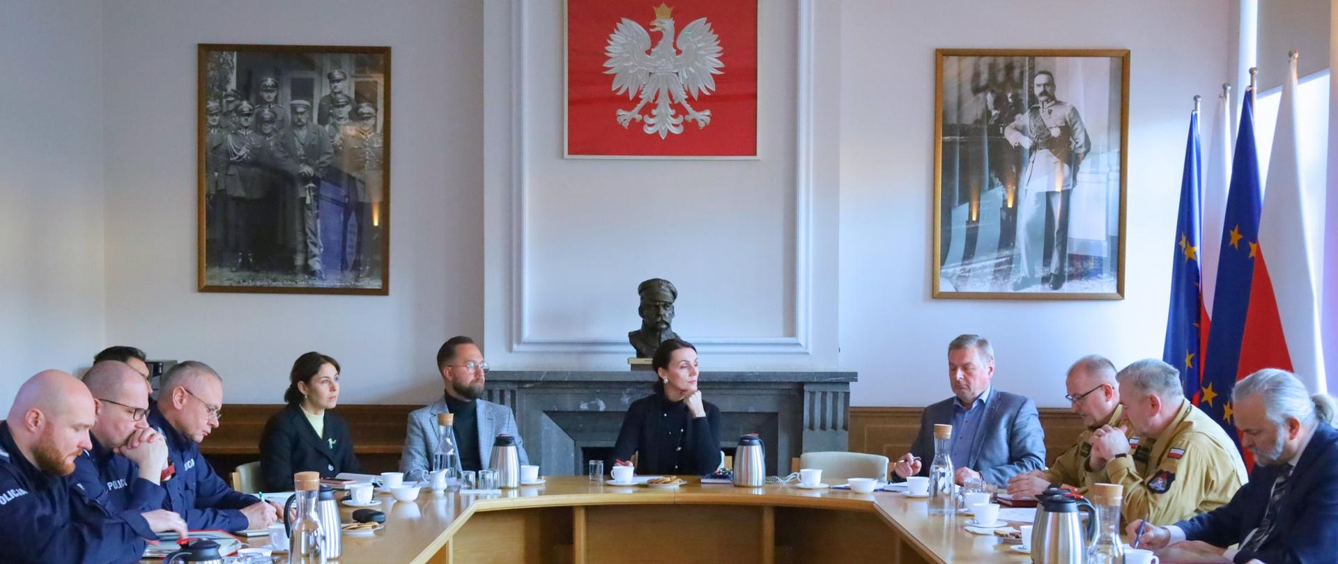 kilkanaście osób siedzi przy okrągłym stole i dyskutuje