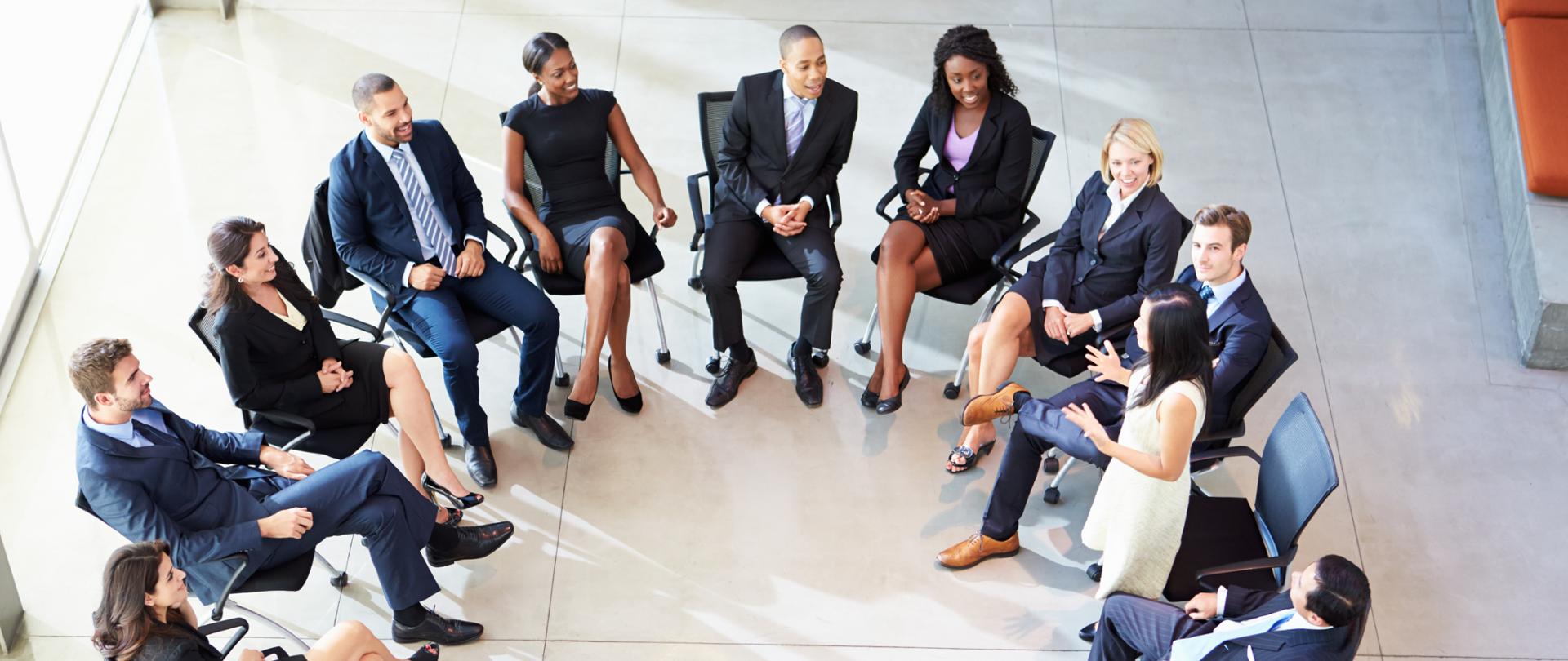 Zdjęcie przedstawia grupę ludzi siedzących na krzesłach w kole.