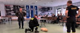 Zdjęcie przedstawia strażaków w trakcie warsztatów z pierwszej pomocy dla nauczycieli.
W tle pomieszczenie świetlicy.
