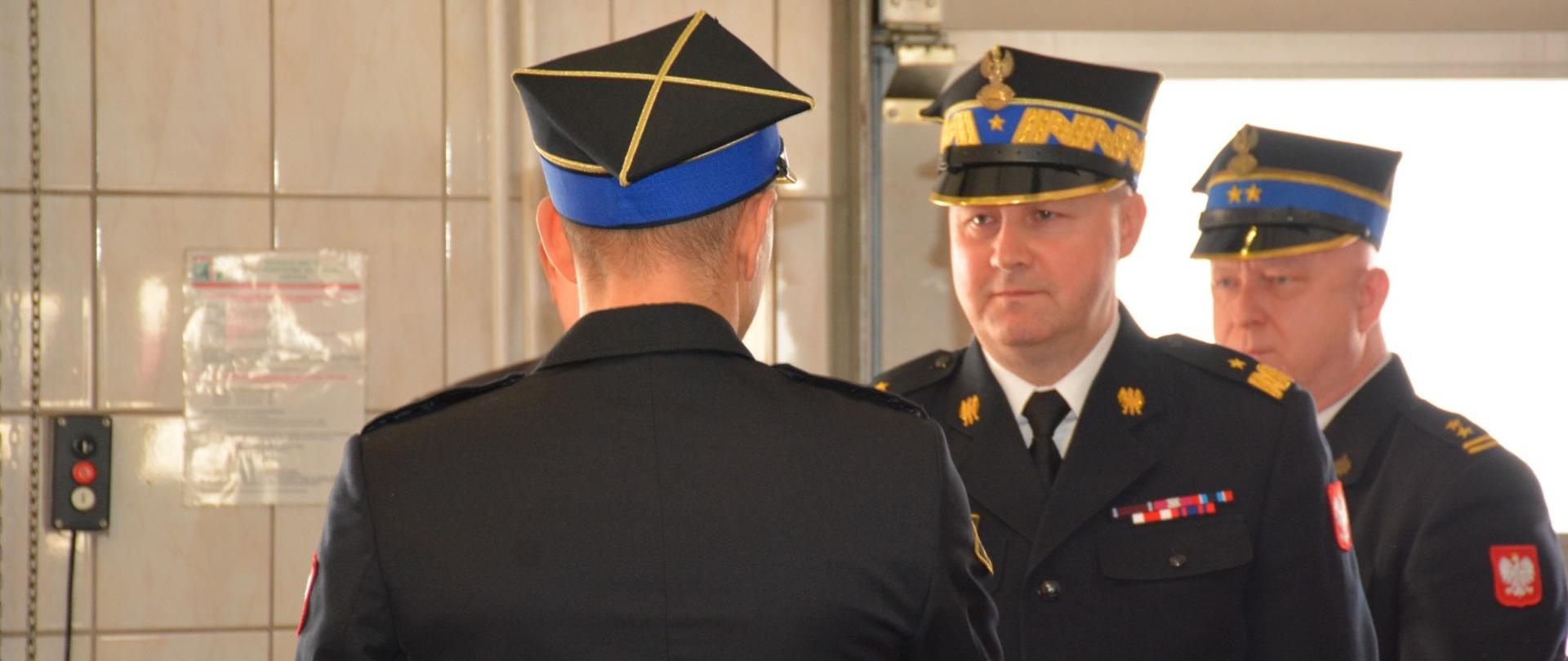 trzech strażaków w garażu ubrani w mundury wyjściowe i rogatywki