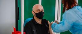 Zdjęcie przedstawia zastępcę świętokrzyskiego komendanta wojewódzkiego PSP podczas szczepienia na COVID-19.