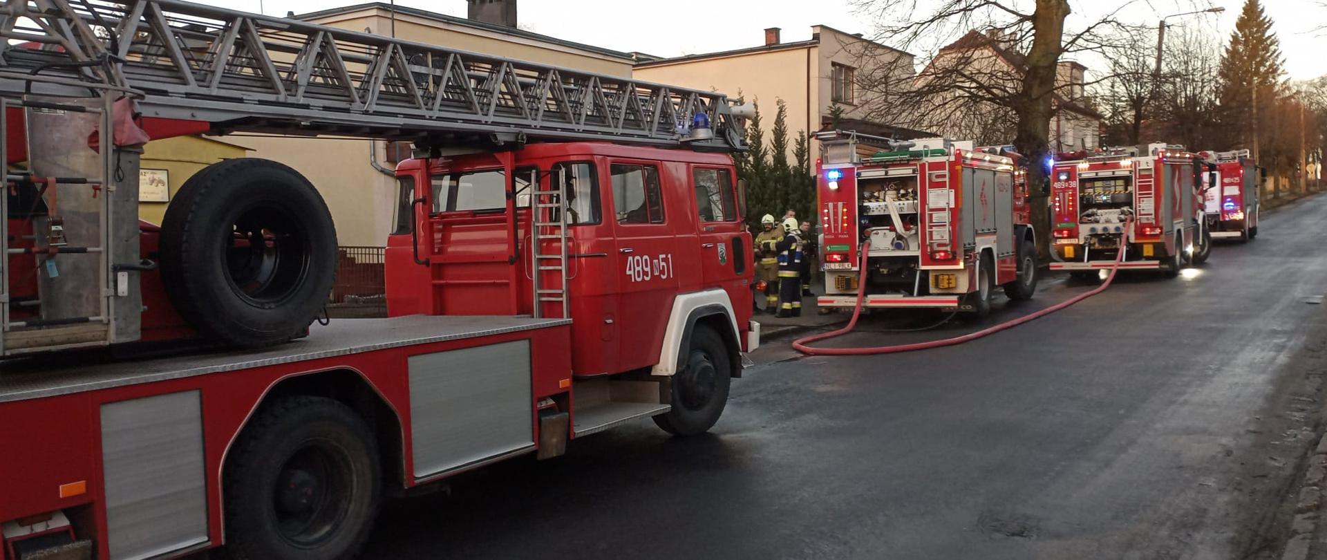 Zdjęcie przedstawia cztery pojazdy pożarnicze w tym drabinę SD30. Zastępy ustawione równolegle do chodnika i domu, w którym miał miejsce pożar w części podpiwniczonej gdzie znajdowała się kotłownia