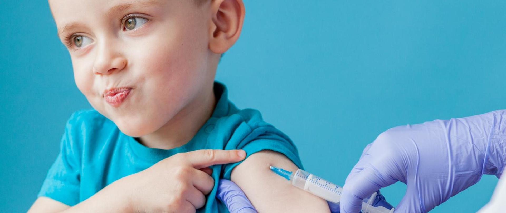 Vaccination concept. Female doctor vaccinating cute little boy on blue background, closeup.