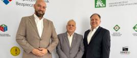 3 mężczyzn pozuje do zdjęcia na tle białej ścianki z logo różnych firm 