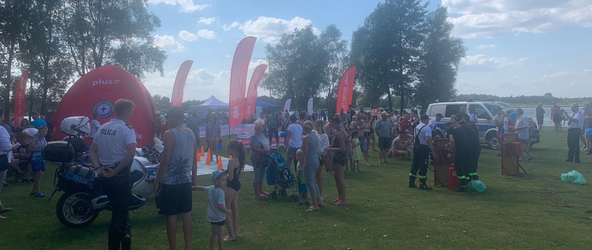 Na zdjęciu widać, przy stoiskach służb i instytucji' uczestników festynu kręci mnie bezpieczeństwo nad wodą. W tle Jezioro Gopło.